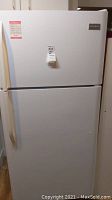 Front view of white Frigidaire refrigerator with top freezer and handles visible. Refrigerator has a tag with the lot number attached to the upper door.