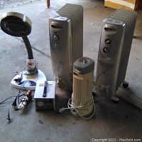 Full lot view showing two oil-filled radiator heaters, Kaz Inc tower heater, Korean heat lamp, transformer, and hair iron on floor.