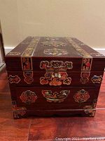 Closed wooden jewelry box showing front with one drawer, ornate inlays, and metal drawer handle