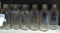 Wide view showing seven of the eleven clear glass milk bottles lined up in a row.