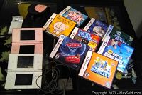 Two Nintendo DS Lite handheld consoles in pink and white with charger, carry case, and eight game cases arranged on table.