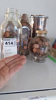 Photo showing five jars of pennies with various shapes and volumes, one labeled for U.S. coins