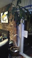 Tall artificial plant in ceramic planter set against brick wall and sliding glass door.