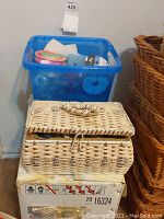 Woven sewing box on top of a cardboard box and blue plastic storage bin containing sewing notions.