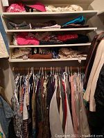Closet shelf and hanging rack filled with assorted women's clothing such as jackets, sweaters, and tops in various colors and fabrics.