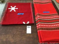 Photo showing folded red rectangular tablecloth with white snowflakes on corners and red stitched border, alongside the red patterned table runner spread lengthwise.