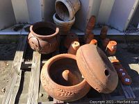 Various clay pots and two clay hose holders arranged on wooden pallets outdoors.