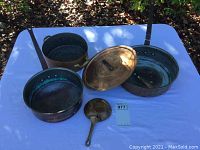 Front view of four copper pots including one with lid and a copper ladle on white cloth.