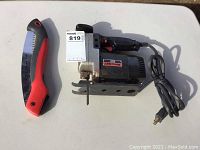 Craftsman scroll saw with razor tooth blade and black and red folding saw laid flat on white surface, power cord visible