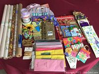 Full view of the gift wrapping assortment showing rolls of wrapping paper, gift bags, ribbons, and tissue paper set on a red surface.