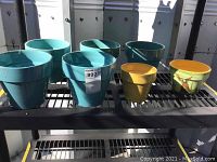 Photo showing 7 glazed garden pots, mostly teal, with one yellow pot and one hand-painted pot with bunny design.
