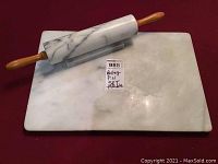 Photo showing marble rolling pin with wooden handles resting on a rectangular marble pastry board with label indicating lot number and description.