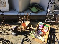 Metal garden art pieces including hanging baskets, decorative metal garden stakes, a small terracotta pot, and a wooden box with garden gloves and supplies. Also a pair of green Sloggers gardening shoes size 8.