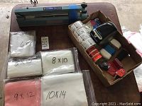 Overview of assortment showing plastic bags bundles labeled with sizes 6x9, 8x10, 9x12, 10x14, moving paper stack, and some packing items in box