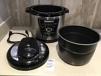 Full view of the electric pressure cooker disassembled showing the base unit, lid, and inner pot arranged on a countertop.