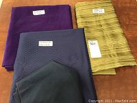 Three folded rectangle tablecloths: purple, greenish-yellow striped, and dark blue dotted, labeled with sizes.