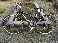 Side view of black Trek 7700 Multitrack ladies bike with tires, seat, pedals, suspension fork visible, sitting on gravel.