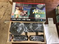 Two boxes of Outdoor Motion Monitor packages open showing black motion sensors and floodlight fixtures, sealed in plastic with instruction manuals included.