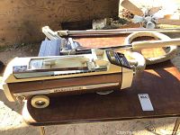 Full side view of vintage brown Electrolux Olympia vacuum cleaner with attached hose and powerhead placed on a wooden table.
