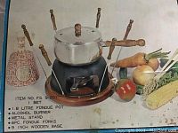 Vintage fondue set displayed with fondue pot on metal stand with wooden base, alcohol burner, and vegetables in background. Close-up of the setup and item details shown on box.