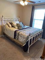 Full view of the queen bed assembled with linens and pillows, located in a bedroom with window and ceiling fan.