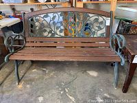 Full front view of outdoor bench showing wood slats seat and backrest with ivy leaf metal design in the backrest, iron arms and legs.