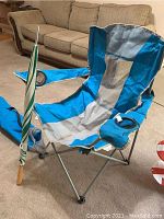Full camping chair with fabric cover and umbrella in blue, grey, green and white stripes placed indoors