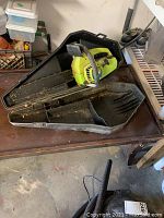 Full shot of Poulan 2000 chainsaw resting in open black plastic carrying case, placed on metal table in garage.