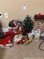 Overview of Christmas decorations including mugs, ornaments, small tree and figurines arranged against wall