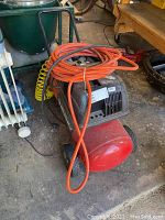 Overall view of Husky air compressor with orange air hose and yellow coiled hose on concrete garage floor.