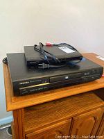 Toshiba and Sony DVD players stacked on a wooden table, showing front panel and power cords.