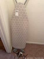 Minky ironing board with hexagonal patterned gray and white cover, metal frame with iron rest, visible power cord for iron.