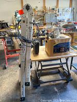 Full view of Gorilla 4-in-1 adjustable ladder folded and standing upright in workshop setting next to table and garage items.