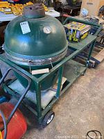 Side view of green ceramic Big Green Egg grill seated on green steel cart with wheels and wooden handle