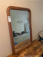 Front view of rectangular vertical mirror with rounded wooden frame against a wall, clear reflective glass.