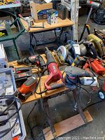 Tabletop view of assorted power tools including Ryobi sander, red hand sander, drills, circular saws