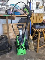 Full view of green Portland electric pressure washer with black hose coiled on the right side and spray gun wand attached on the left running upward with green trigger handle.