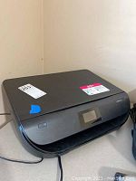 Front view of the black HP ENVY 5055 printer showing its overall shape, small LCD touchscreen, and paper input lid closed.