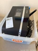 Clear plastic tote containing Sirius XM radio kit items including docking station, radio receiver, and cables