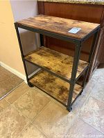 Front angle view showing top and two lower wood shelves supported by black metal frame and casters.