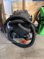 Front view of black Shop-Vac with attached hose, showing dust and dirt, situated in garage.
