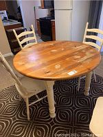 Overall view of round wooden table with four white painted chairs placed around it, showing use and wear on surfaces.
