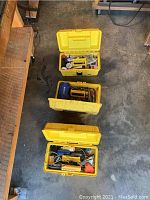 Top-down view of three yellow plastic toolboxes filled with assorted small tools and hardware items, set on a concrete floor.