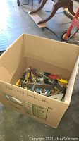 Photo showing top view of a box filled with various pliers, pipe cutters, screwdrivers, and other mixed hand tools, confirming variety and quantity of items.