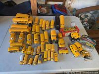 View of over 30 yellow toy school buses and related vehicle toys arranged on table.