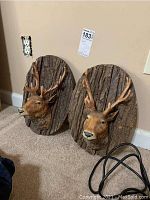 Pair of mounted deer head wall art with bark-textured oval wood plaques shown placed on floor against wall.