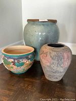 Three pottery jardinières arranged on floor, varying sizes and colors