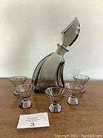 Full view of the smoky glass decanter with stopper and surrounding five shot glasses on a wooden surface.