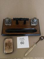 Wooden desk stand featuring two glass inkwells with metal lids, a black pen rest area, clear glass paperweight with embedded sepia photograph, and small ornate letter opener with cross detail