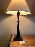 Full view of the lamp lit showing fabric shade and bronze tapered base.